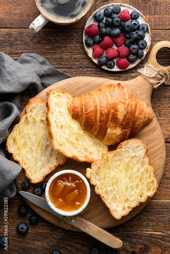 French croissants with berries and jam on a wooden background, top view. Halved croissants, croissant texture