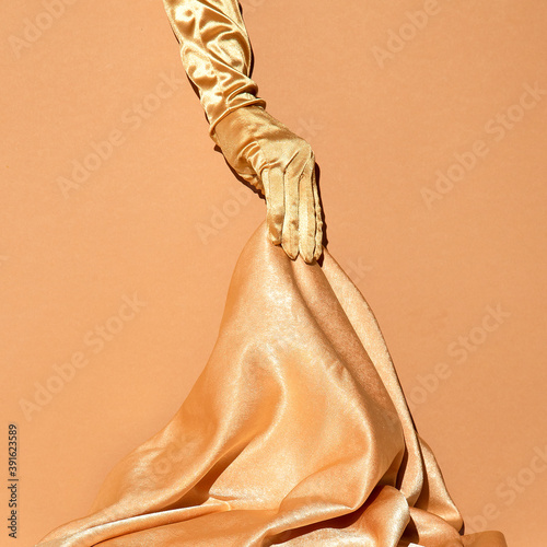 Hand in golden gloves holds golden textile. Holiday,christmas, birthday concept. Still life fashion wallpaper