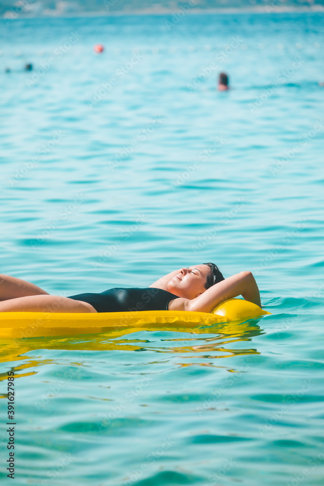 beautiful sexy woman laying on yellow inflatable mattress at sea water