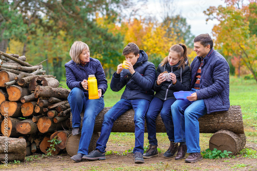 family relaxing outdoor in autumn city park  happy people together  parents and children  they drink tea and eat sandwiches  talking and smiling  beautiful nature