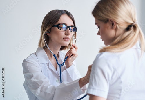Woman cleaning lady in a medical gown listens to the patient's heartbeat on a light background