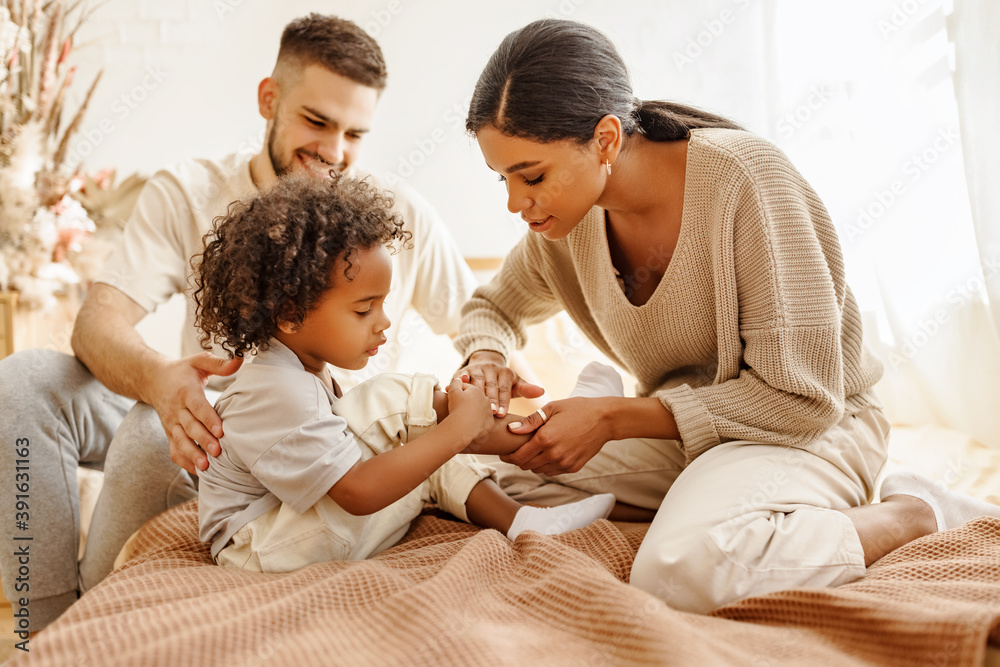 happy multi ethnic family mother feels sorry for baby who hurt leg in bed   at home.