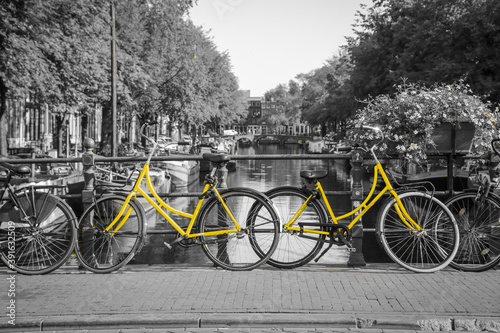 Two fresh yellow bikes on the streets of Amsterdam. Symbol for clean and ecological urban transport. Isolated in a black and white background.