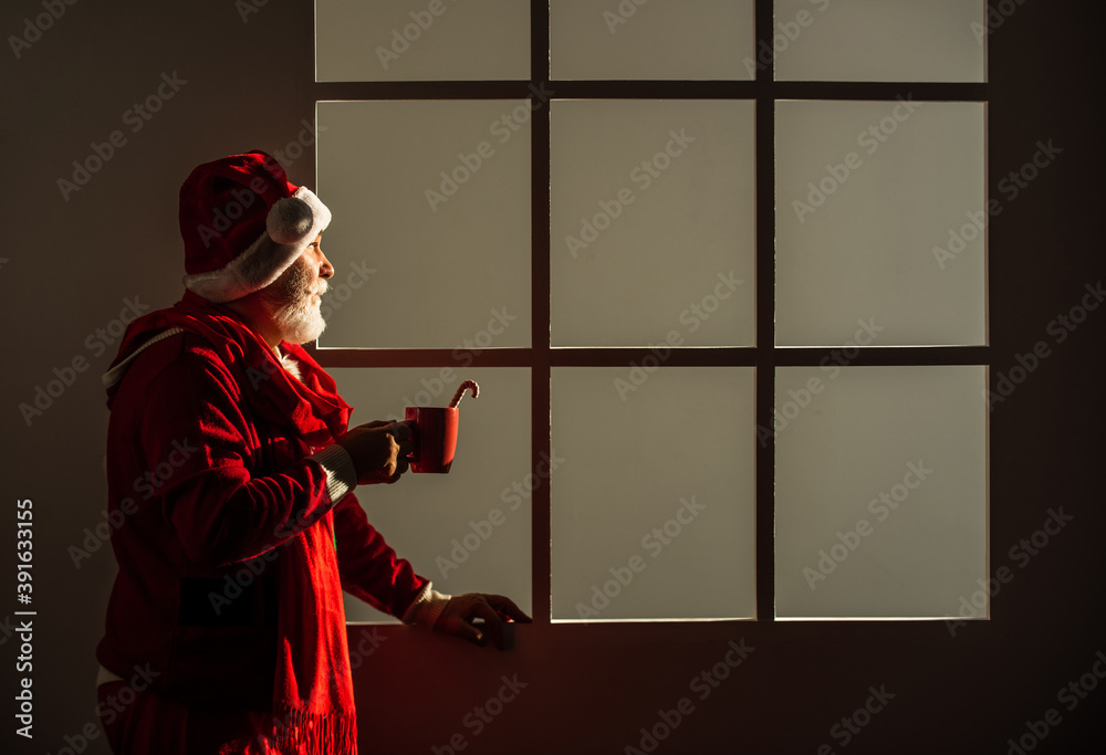 Naklejka premium man in santa hat drink milk or cocoa with stick. The morning before Xmas. enjoy the winter holiday. delivery new year gifts. Christmas online shopping. santa claus with white beard