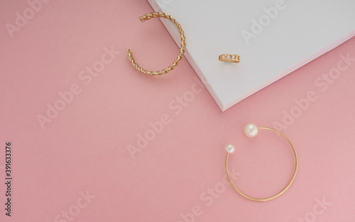Top view of golden jewelries on pink and white background with copy space