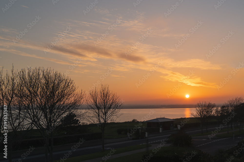 Fototapeta premium Sunset over Pegwell Bay. The trees, grass and road of the west cliff Royal Esplanade are in the foreground.