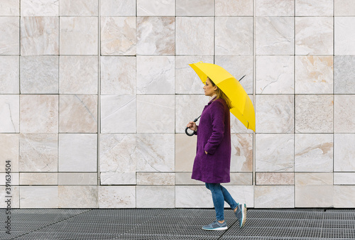Woman walking with a yellow umbrella on a stone architecture background