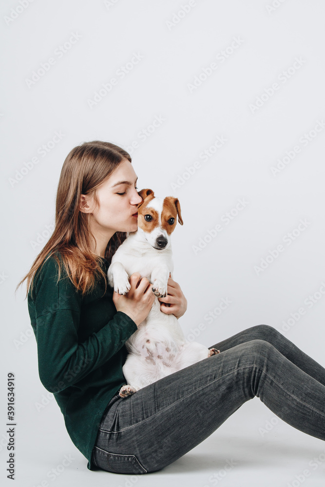 Cute young woman kisses and hugs her puppy jack russell terrier dog. Love between owner and dog. Isolated on white background. Studio portrait. Cute young woman kisses and hugs her puppy jack russell terrier dog. Love between owner and dog. Isolated on white background. Studio portrait.