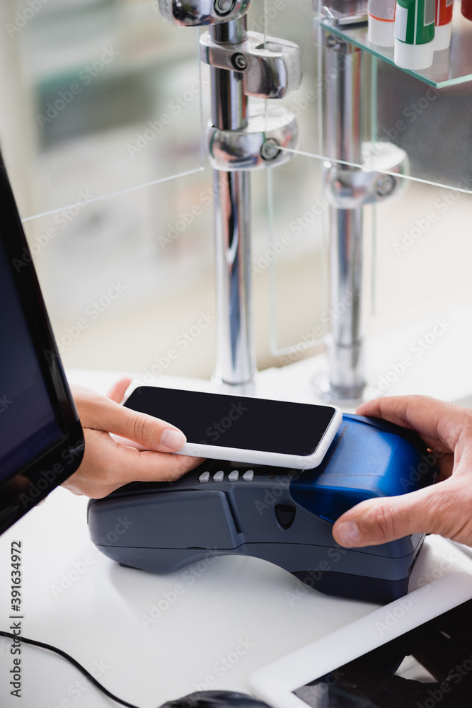 cropped view of woman holding smartphone over payment terminal in drugstore cropped view of woman holding smartphone over payment terminal in drugstore
