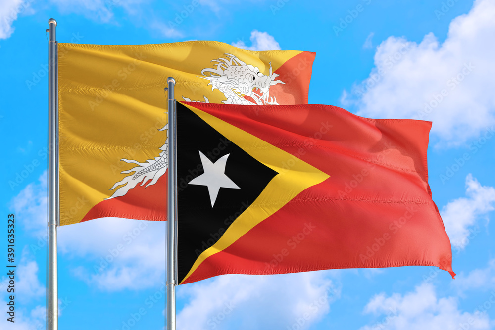 East Timor and Bhutan national flag waving in the windy deep blue sky. Diplomacy and international relations concept. East Timor and Bhutan national flag waving in the windy deep blue sky. Diplomacy and international relations concept.