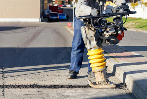 A road builder uses a vibration rammer to repair an asphalt road section. photo