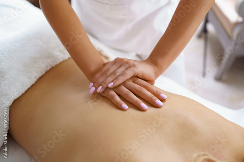 Professional massage therapist massages the back of adult woman lying on massage table, close-up. Lady gets relaxing massage. Concept of body care.