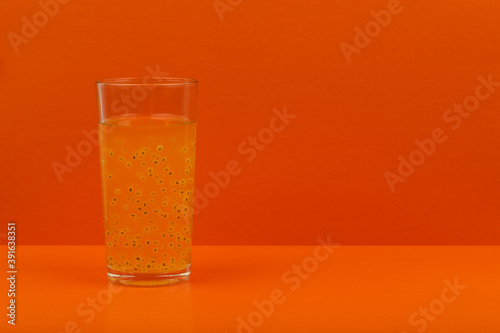 Glass of fruit orange juice with passion fruit seeds on orange background with space for text