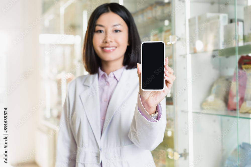 smartphone with blank screen in hand of cheerful asian pharmacist in white coat on blurred background smartphone with blank screen in hand of cheerful asian pharmacist in white coat on blurred background