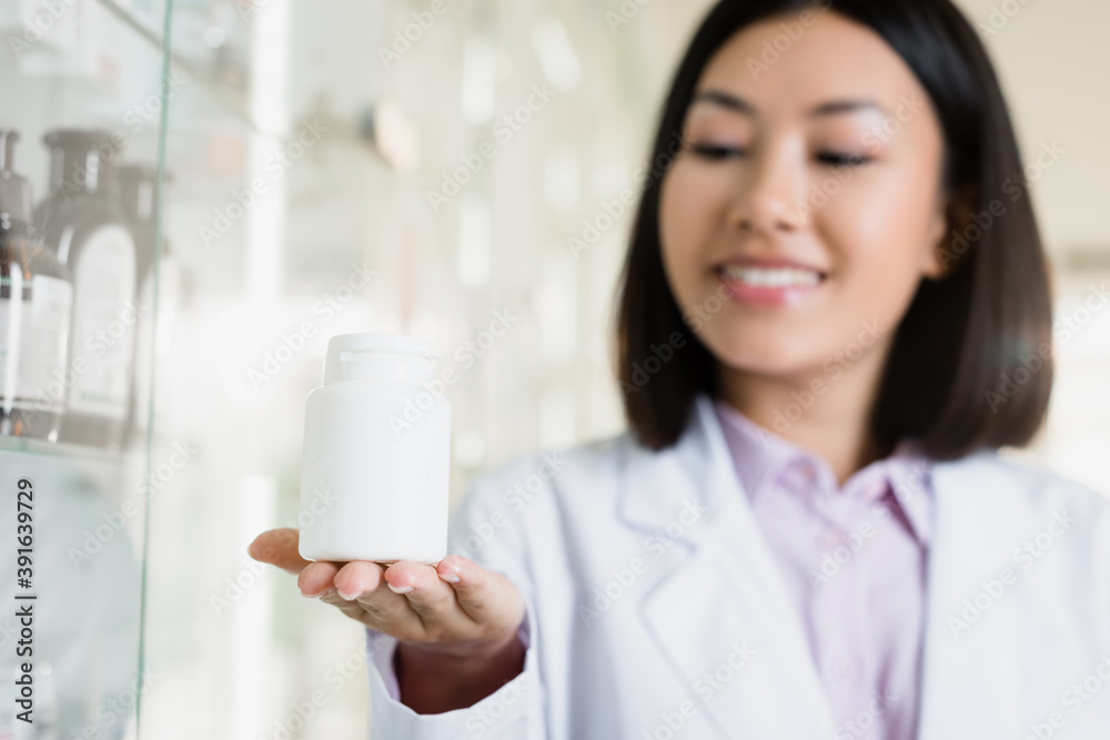 bottle with medication in hand of cheerful asian pharmacist on blurred background bottle with medication in hand of cheerful asian pharmacist on blurred background