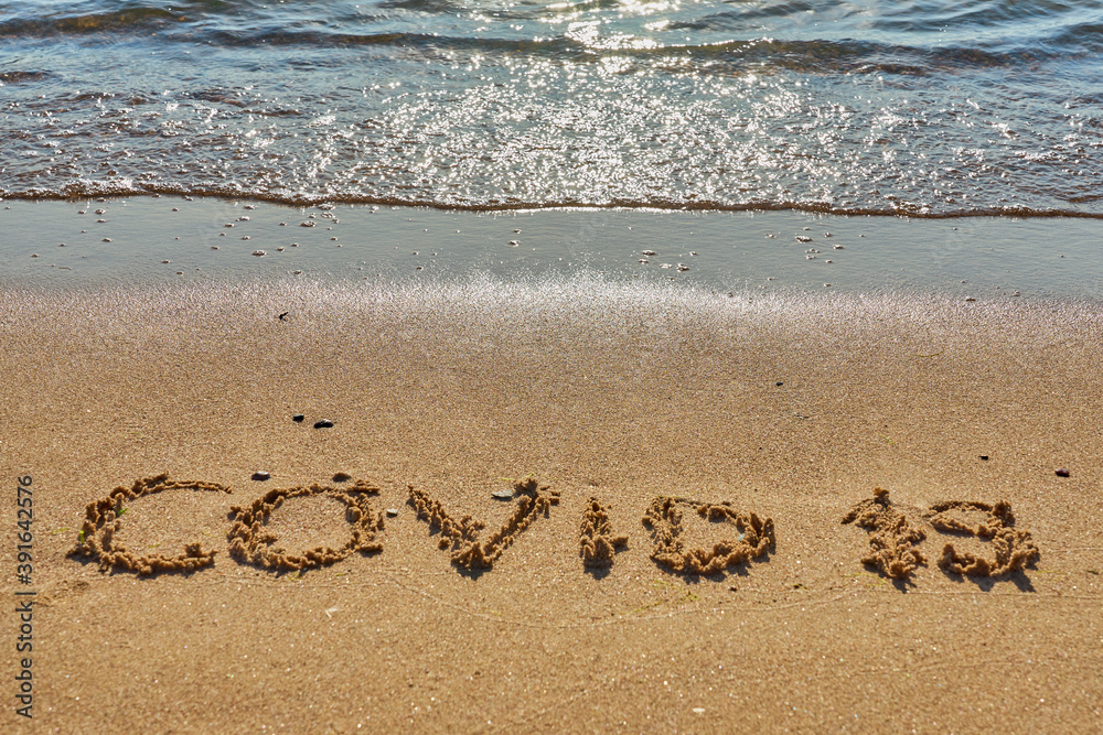 Covid 19 inscription on a tropical sandy beach with waves and foam on a background. Covid 19 inscription on a tropical sandy beach with waves and foam on a background.