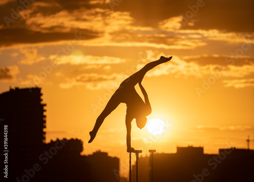 Flexible acrobat doing handstand on the cityscape background during dramatic sunset. Concept of willpower, control and dream