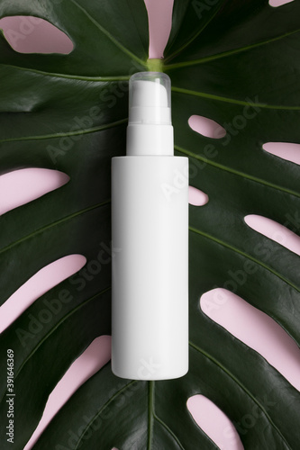 Top view of a white cosmetic lotion bottle mockup with a monstera leaf on a pink background.