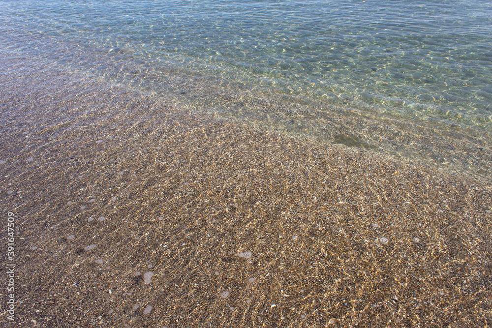 Transparent clean blue sea water surface with brown sand beach into sun reflection   