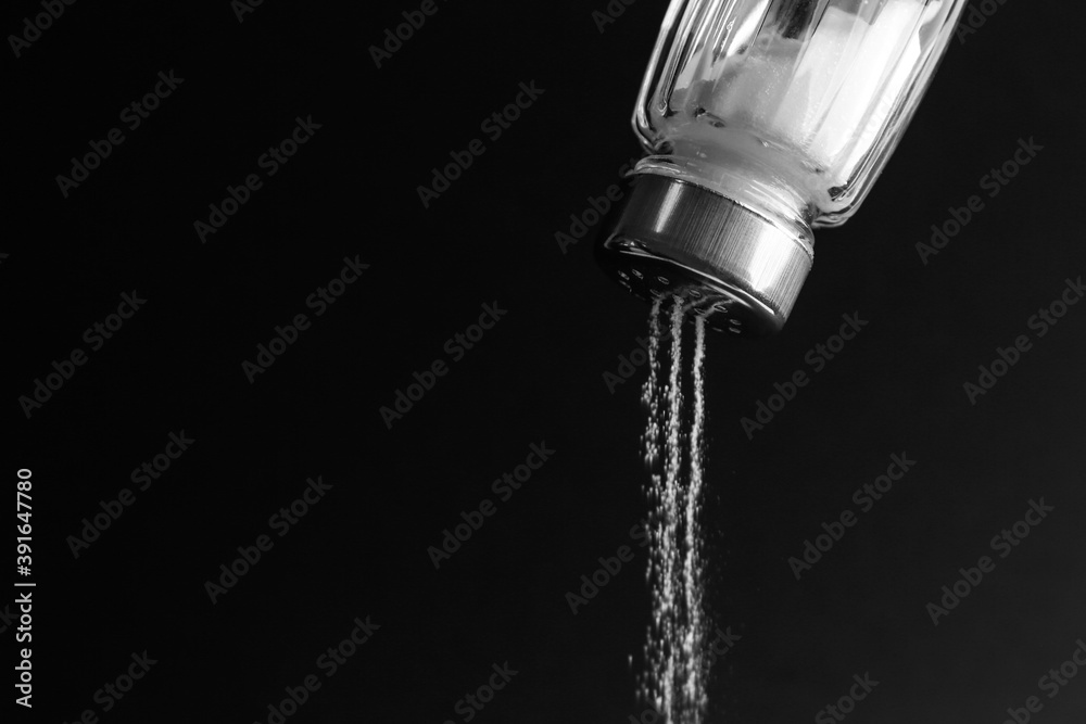 Pouring salt from shaker on black background, closeup. Space for text Pouring salt from shaker on black background, closeup. Space for text