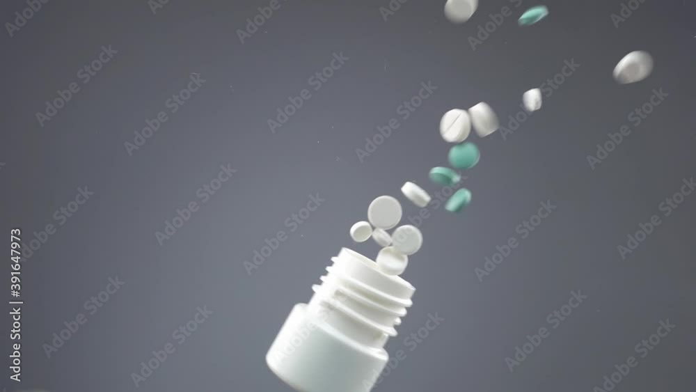 A hand in glove throws a plastic container with pills and they spills on glass surface in slow motion. A flying jar with drugs is seen from below on grey background. Theme of medicine and healthcare. A hand in glove throws a plastic container with pills and they spills on glass surface in slow motion. A flying jar with drugs is seen from below on grey background. Theme of medicine and healthcare.