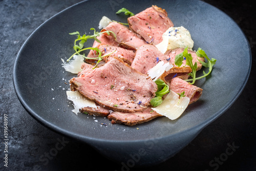 Modern style traditional lunch meat with sliced cold cuts roast beef with rocket salad and parmesan cheese served as close-up in a design plate