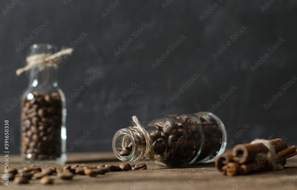 Stilllife with bottles filled by coffee beans on the black background with scattered coffee beans and cinnamon Stilllife with bottles filled by coffee beans on the black background with scattered coffee beans and cinnamon
