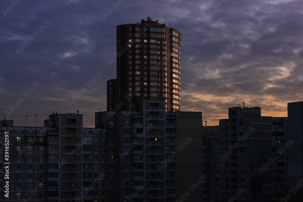 Tall red brick building and many other houses behind it against the background of a purple orange pre-sundown sky in the evening. Modern architecture Kiev, Ukraine Tall red brick building and many other houses behind it against the background of a purple orange pre-sundown sky in the evening. Modern architecture Kiev, Ukraine