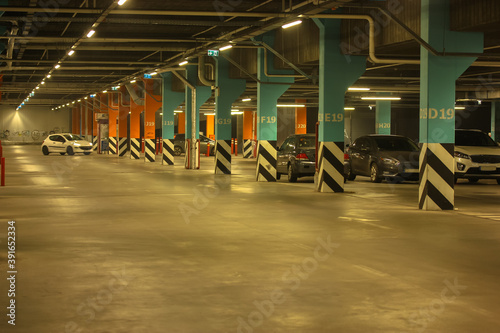 Well-lit parking with easy navigation in the mall with many cars in the evening, gray concrete road for traffic and separating numbered poles 