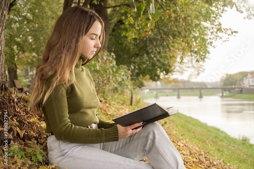 A young girl reads a book on the autumn waterfront