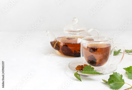 Organic chaga tea in a glass cup and teapot. Infusion with pieces of birch mushroom on a white background.
