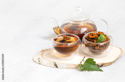 Chaga mushroom drink in glass bowls and teapot on a white background. Healthy infusion with pieces of chaga.