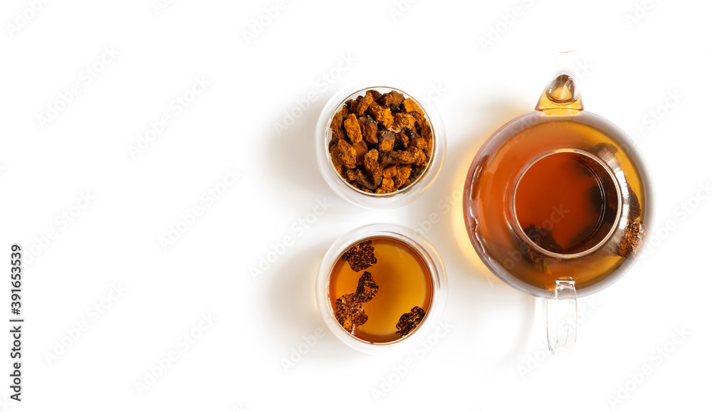 Chaga tea and chaga mushroom pieces in glass bowls and teapot isolated on a white background. Copy space, top view, flat lay.