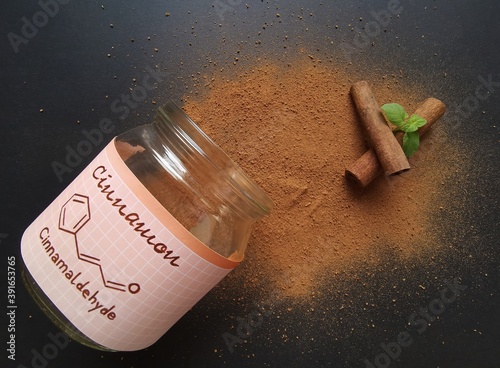 Fototapeta Naklejka Na Ścianę i Meble -  Cinnamon sticks and milled cinnamon spice in the glass jar with structural chemical formula of cinnamaldehyde (the major component of cinnamon). Winter spices, cinnamon sticks and cinnamon powder.