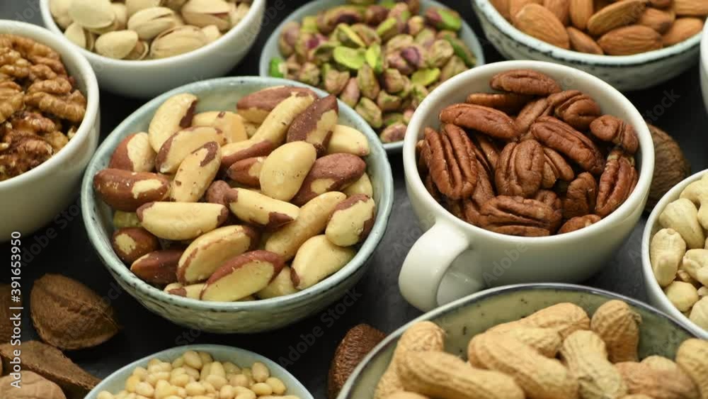 Assortment of various nuts in bowls and cups, top view on black, stone background Assortment of various nuts in bowls and cups, top view on black, stone background