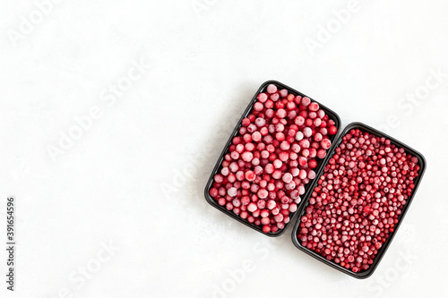 Frozen berries in plastic containers on a white background. Storage of frozen food. Cranberries and cowberries. Copy space, top view
