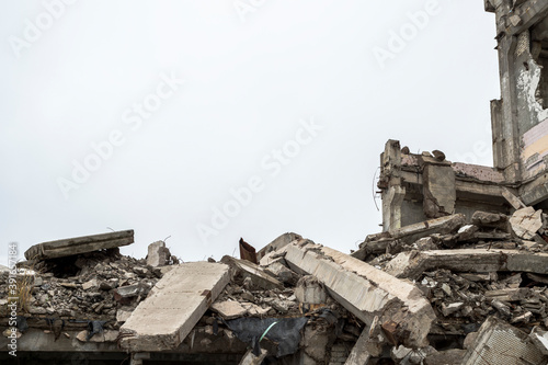 A ruined building with a pile of concrete gray debris against a neutral gray sky in a hazy haze. Background