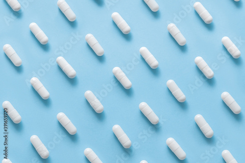 Scattered Pills on a blue background , Medicine concept. Multiple long white capsules on a blue. Pattern of capsules on a blue. Minimalism background