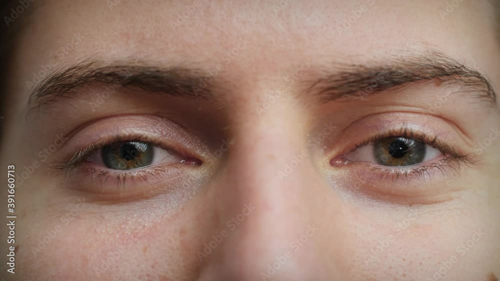 Close up of Man's face. Attractive boy with blue eyes raising eyebrows. Concept of flirting, joking, funny. Male model with pretty blue, green, grey eyes. Slow-motion, macro extreme close-up, 4K.