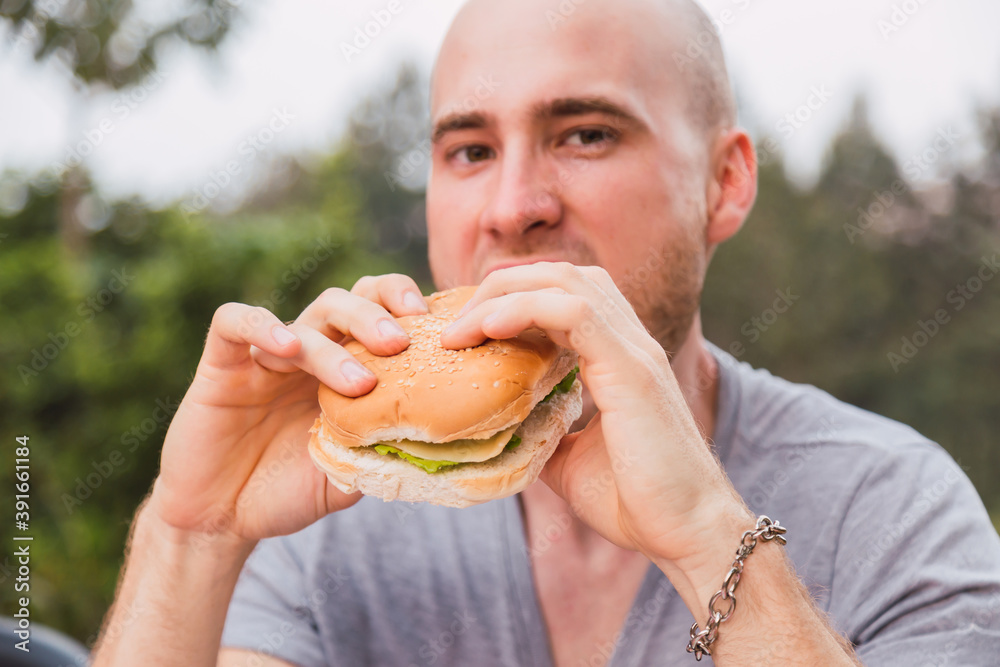 A handsome man holding a hamburger - The handsome young man wanted to try his delicious cheeseburger. A handsome man holding a hamburger - The handsome young man wanted to try his delicious cheeseburger.