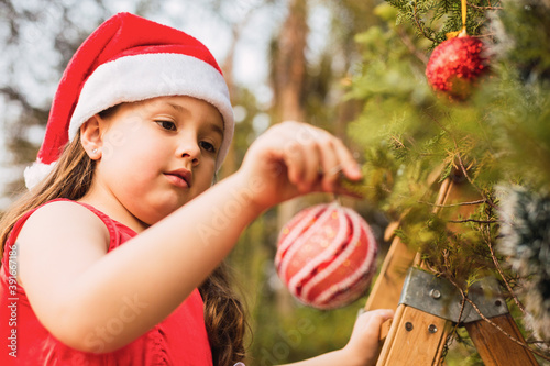 Adorable girl decorating the Christmas tree. Pretty little girl choosing the Christmas tree decoration