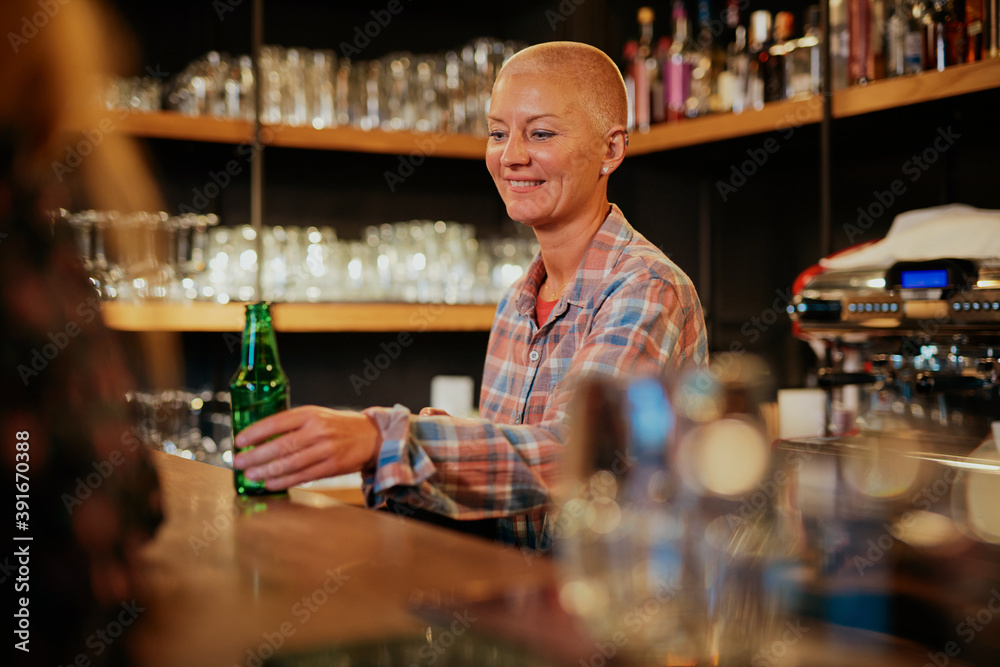 Smiling waitress standing in a bar and serving beer.