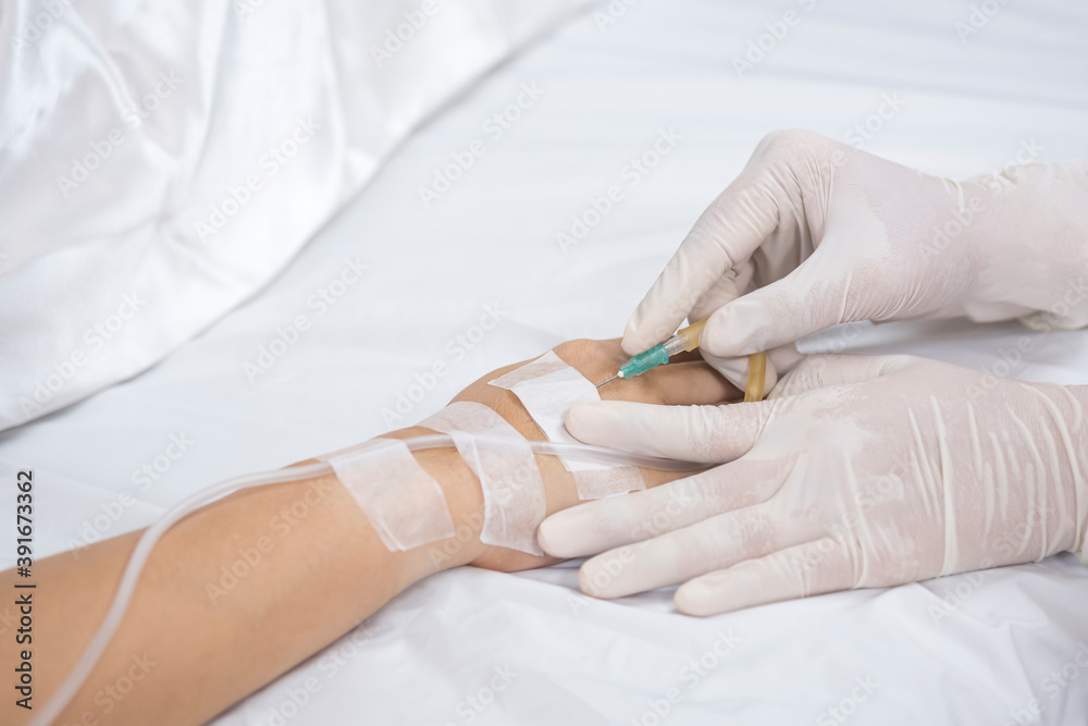 Fototapeta premium Close up doctor's hand injects saline infusion needle into patient on bed 