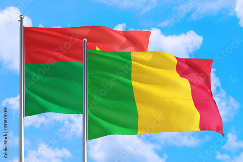 Mali and Burkina Faso national flag waving in the windy deep blue sky. Diplomacy and international relations concept.