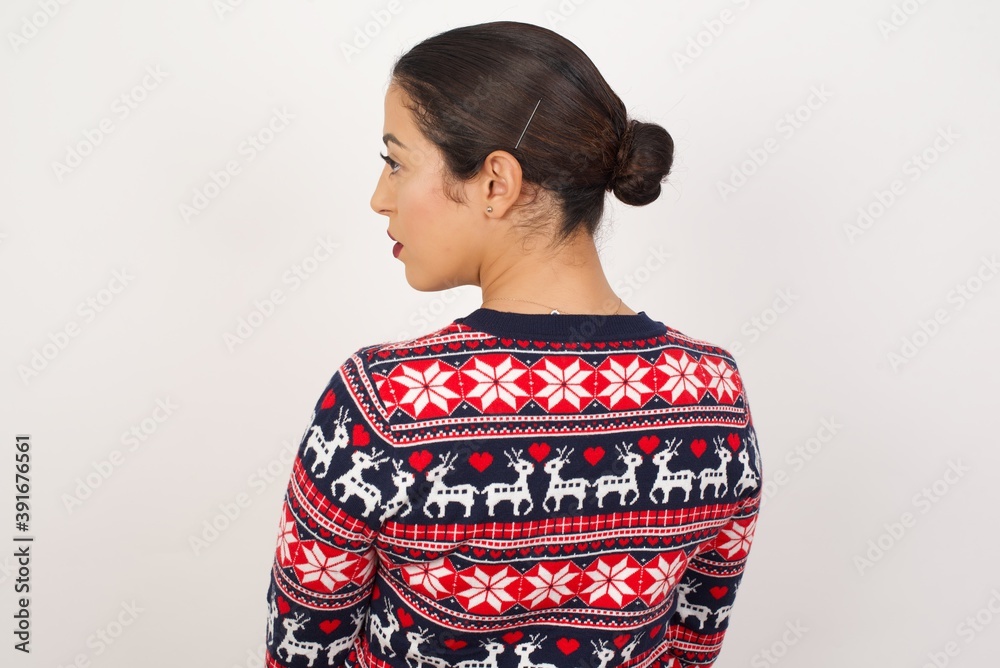 The back side view of a Young beautiful Arab woman wearing Christmas sweater against white wall,  Studio Shoot.