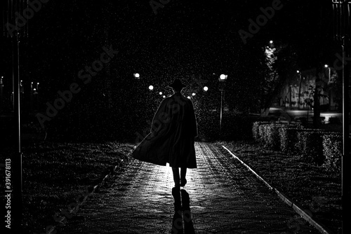 Fotografie dark silhouette of a male detective in a coat and hat in the rain on a night str