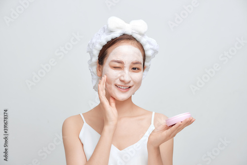Beautiful young woman with towel wrapped around her head applying face mask