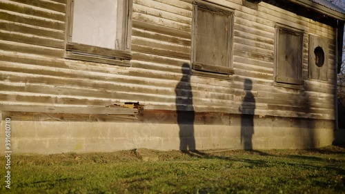 Two people's shadows having a conversation outside of a dilapidated, abandoned farm house in autumn. photo