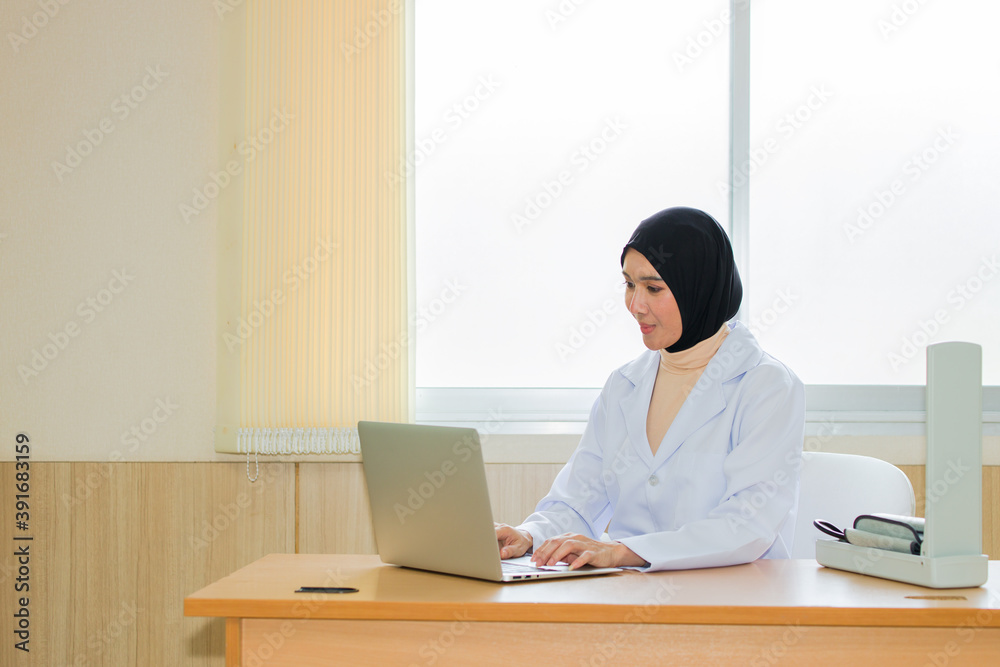 Arab female doctor using laptop in examination room. Arab female doctor using laptop in examination room.