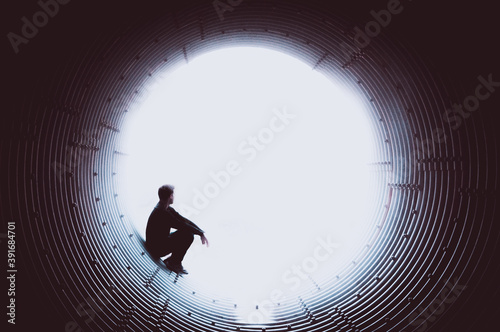 Silhouette of a man looking pensively at the edge of a tunnel through a white void. Space to place text. Concept